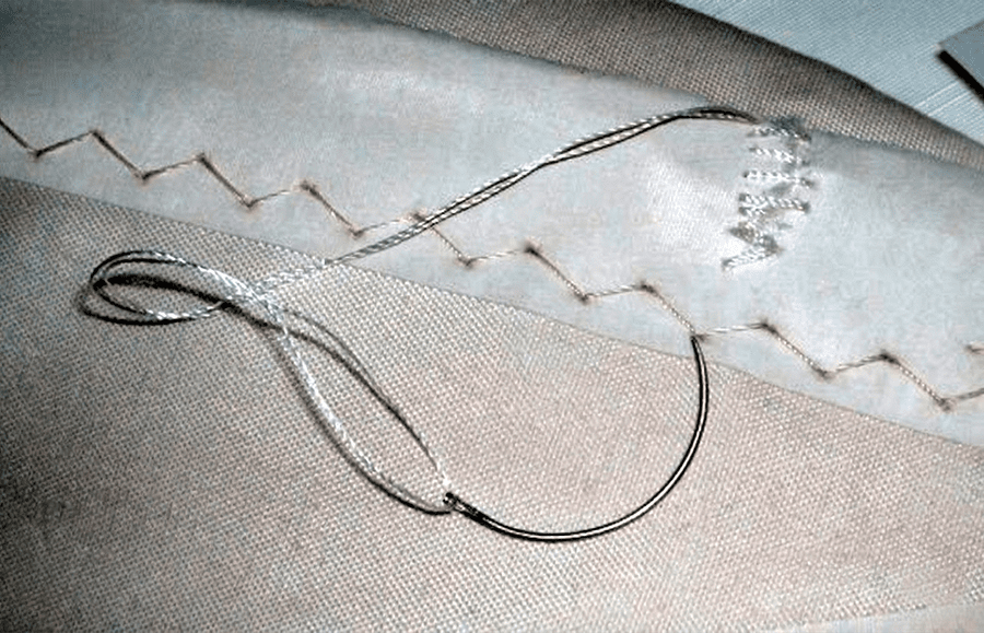 Detalle de costura reconstruida en zigzag sobre vela de Dacron, mostrando los orificios originales y las dos pasadas cruzadas.