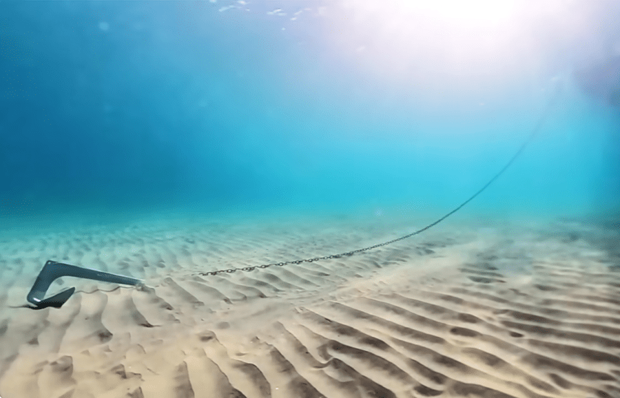Vista submarina: ancla Bruce con cadena plana en fondo de arena subiendo hacia la superficie