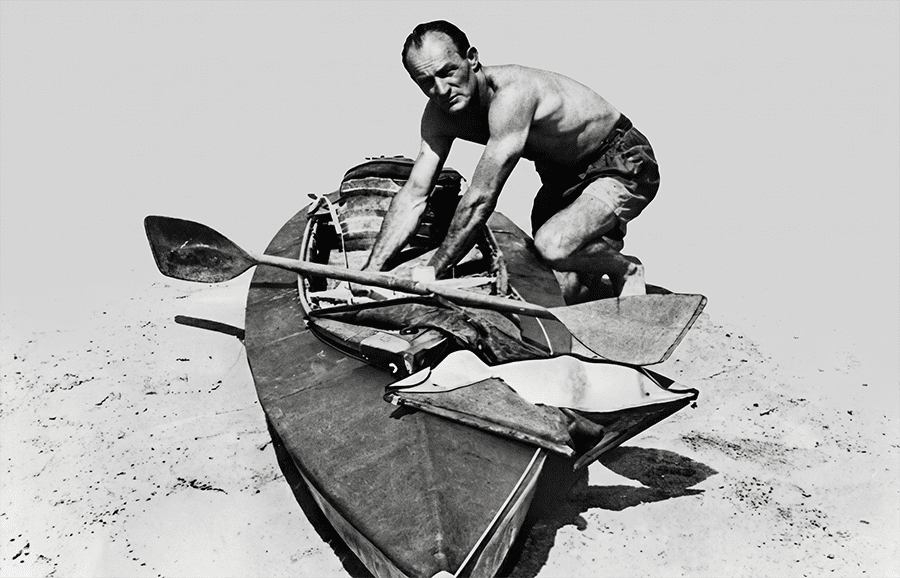 Oskar Speck arrodillado junto a su kayak plegable Faltboot sobre la arena