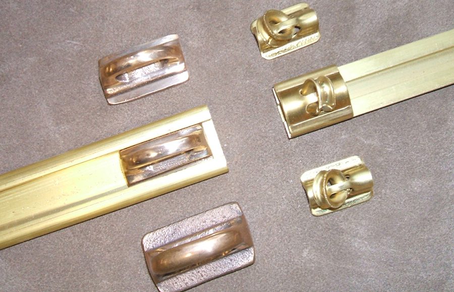 Riel exterior e interno de bronce con sus respectivos patines y garruchos sobre fondo gris