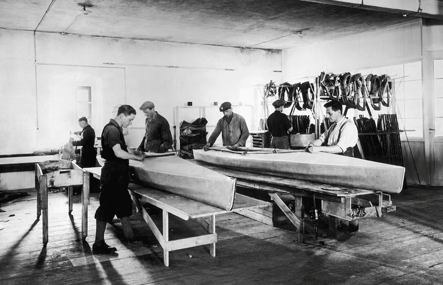 Taller de fabricación de kayaks plegables Faltboot en los años 30, con cascos sobre bancos y pieles colgadas al fondo