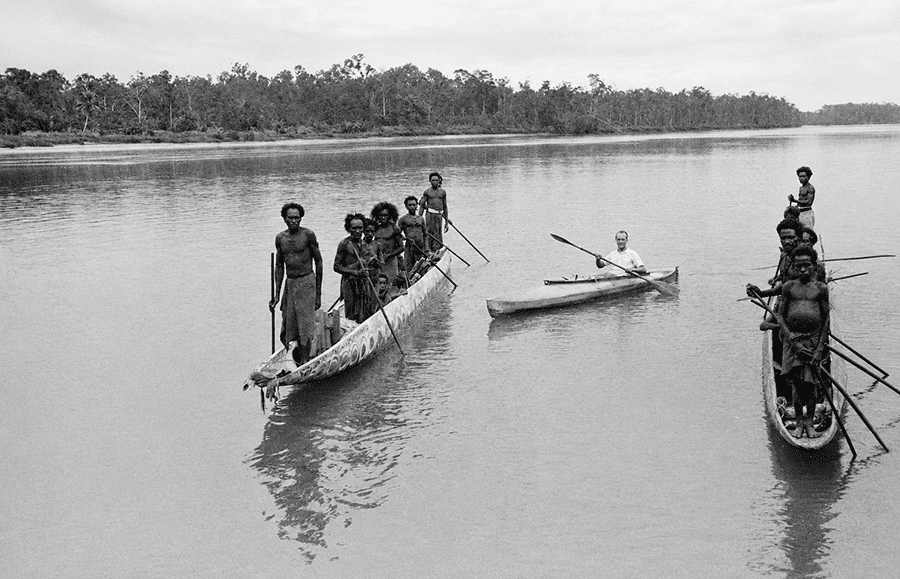 Oskar Speck en su kayak Sonnenschein rodeado de canoas tradicionales excavadas en troncos con pobladores locales, posiblemente en Papúa Occidental