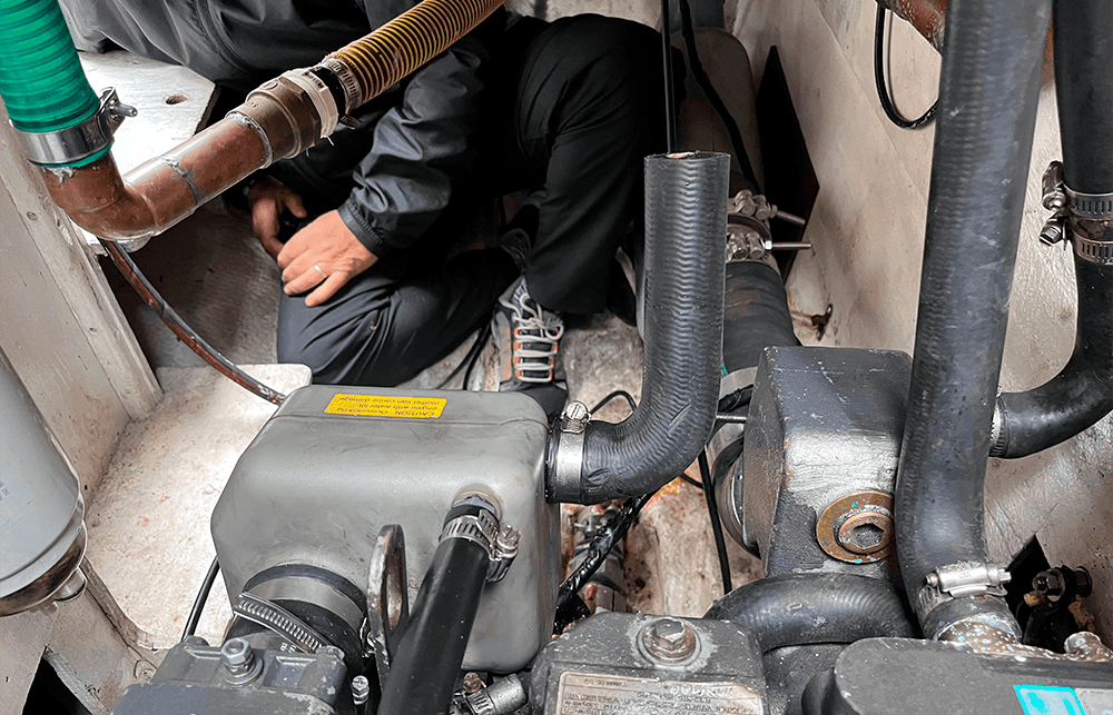 Tripulante agachado en el reducido espacio situado a popa del motor del Lancet, inspeccionando los ramales de los imbornales, sus conexiones y las válvulas de fondo.